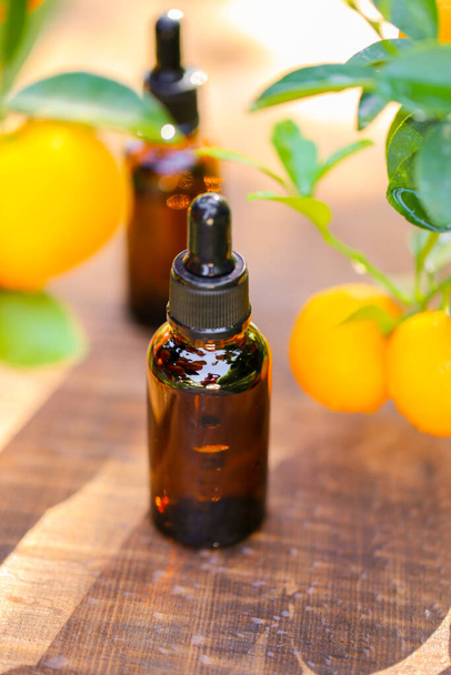 Citrus oil.tangerine essential oil.Natural organic pure oil. brown bottles with oil on a brown wood background and tangerines with green leaves. - Zdjęcie, obraz