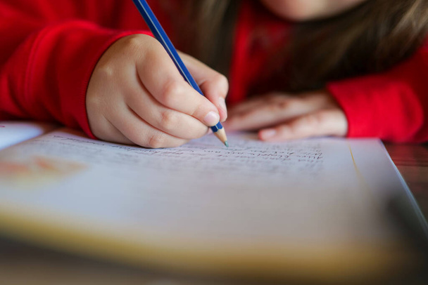 Koulutyttö tekee läksynsä. lapsi kirjoittaa kynällä muistikirjaan.Kotitehtävä.Opiskelu ja koulutus. - Valokuva, kuva