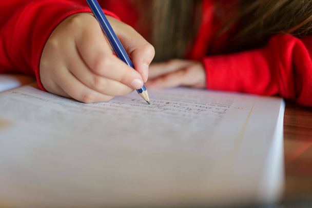Opiskella ja kouluttautua. Koulutyttö tekee kotiläksynsä. lähikuva lyijykynä lapsen kädessä kirjoittaa sanoja muistikirjaan.lapsi kirjoittaa kynällä muistikirjaan.Kotitehtävät. - Valokuva, kuva
