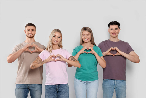 Happy volunteers making hearts with their hands on light background - Fotoğraf, Görsel