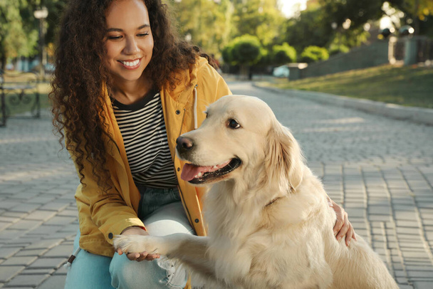 Young African-American woman and her Golden Retriever dog in park - Фото, изображение