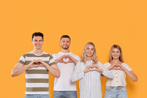 Happy volunteers making hearts with their hands on orange background - Фото, изображение