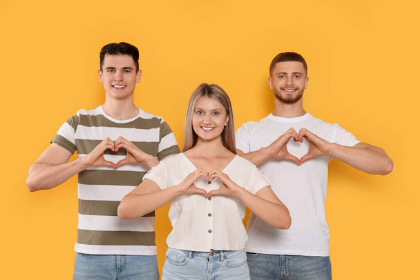 Happy volunteers making hearts with their hands on orange background - Фото, изображение