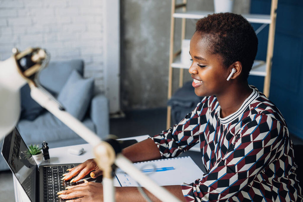 Smiling young African American businesswoman working on a laptop at her desk in office. Remote job, technology and people concept - Zdjęcie, obraz