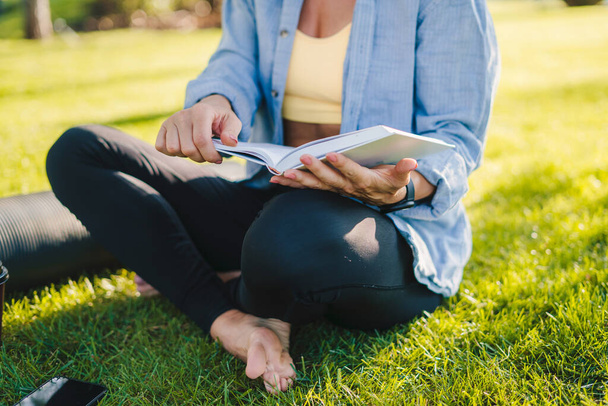 Widok kobiety ubranej w odzież sportową siedzącej w środku parku bez ludzi czytających książkę. Zdrowy styl życia, sport. Mądra dziewczyna patrząc student - Zdjęcie, obraz