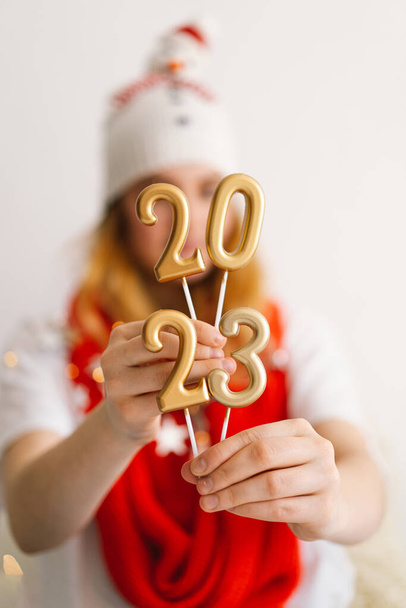 Funny jeune fille dans un chapeau de Nouvel An et écharpe rouge tient les numéros 2023 dans ses mains. Nouvel an et concept de Noël. - Photo, image