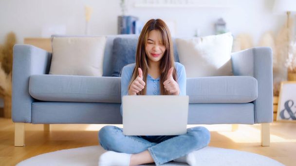 Junge Asiatin, die zu Hause an ihrem Laptop arbeitet und grinst. attraktive Asiatin nutzt Computer für Online-Schulungen, Videotelefonie und Konferenzgespräche - Foto, Bild
