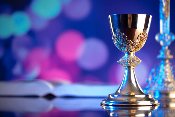Catholic religion concept. Catholic symbols composition. The Cross, monstrance,  Holy Bible and golden chalice on wooden altar and blue bokeh background.  - Photo, Image
