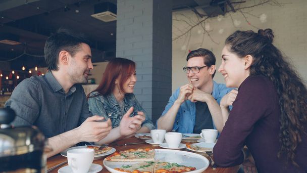 Amigos cercanos están compartiendo historias divertidas haciendo gestos y riéndose mientras almuerzan en la moderna cafetería local. Emociones positivas, gente feliz y sabroso concepto de comida
. - Foto, Imagen