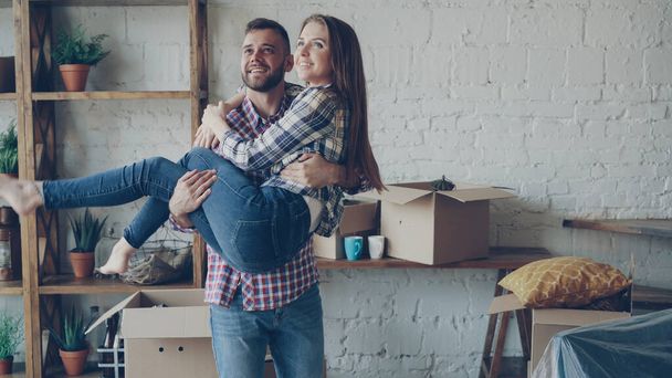 Cheerful strong guy is whirling his girlfriend while moving to new house after purchasing it. Romantic relationship, people and housing concept. - Photo, Image