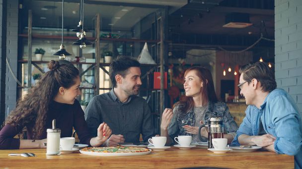 Happy and attractive group of female and male friends are chatting and laughing together in a small modern cafe or pizza house. Communication and food service concept. - Fotografie, Obrázek