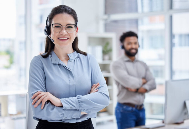 Portrait of one confident young caucasian woman standing with arms crossed while working in a call centre with her colleague in the background. Happy manager and ambitious supervisor determined to pr. - Foto, Bild