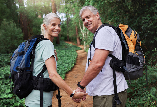 Portret van een volwassen stel dat elkaars hand vasthoudt terwijl ze samen wandelen. Oudere paar glimlachen tijdens een wandeling kijken gelukkig in de natuur. - Foto, afbeelding