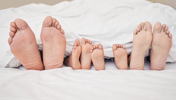 Dichtbij een familie die in bed ligt. Grote voeten van ouders en kinderen die in bed uitsteken. Gezin met twee kinderen ontspannen samen in bed. Kinderen slapen in bed met hun ouders. - Foto, afbeelding
