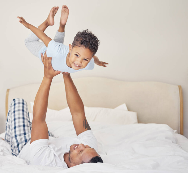 Joyful young single father lying on bed, lifting excited happy little child son at home. Little boy pretending to fly while having fun in bedroom with parent. - Fotó, kép