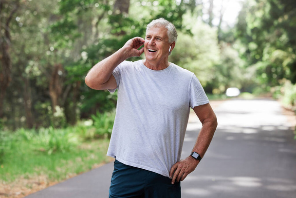 A zene segít átvészelni a futást. egy érett férfi vezeték nélküli fülhallgatót visel, miközben a szabadban gyakorol. - Fotó, kép