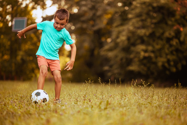 Νεαρό αγόρι παίζει ποδόσφαιρο στο πάρκο.Δράση με μπάλα ποδοσφαίρου.Παιδικό ποδόσφαιρο. - Φωτογραφία, εικόνα
