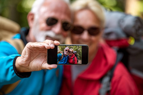 Doğadaki yaşlı çift, selfie çekin ve ormanda yürüyün.. - Fotoğraf, Görsel