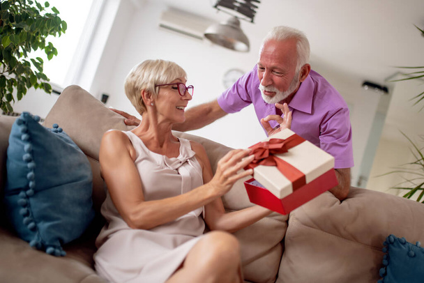 Senior man giving present to his wife. Celebrating holidays together. - Фото, зображення