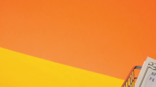 Handschiebender Supermarkt-Einkaufswagen mit 20-Dollar-Schein Geld im Einkaufswagen auf gelbem Hintergrund. Verkaufskorb von US-Dollar-Scheinen. Existenzminimumkonzept: Darlehen, Altersvorsorge ansparen - Filmmaterial, Video