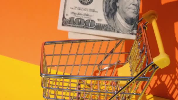 Hand add 100 dollar banknote Money in toy supermarket trolley shopping cart on yellow background. Sales Basket of US dollar bills. Minimum living wage Concept: loan, investment pension saving money - Footage, Video