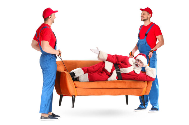 Cargadores masculinos que llevan sofá con Santa Claus tumbado sobre fondo blanco - Foto, imagen