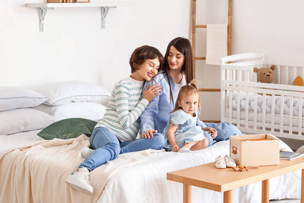 Mladá těhotná žena se svou ženou a malou dcerou sedí na posteli doma - Fotografie, Obrázek