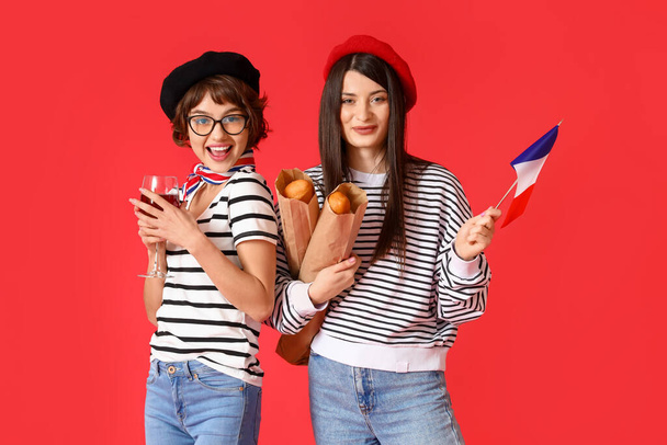 Jovens mulheres com bandeira da França, vinho e baguetes em fundo vermelho - Foto, Imagem