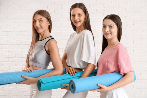 Sporty giovani donne con stuoie yoga su sfondo mattone bianco - Foto, immagini