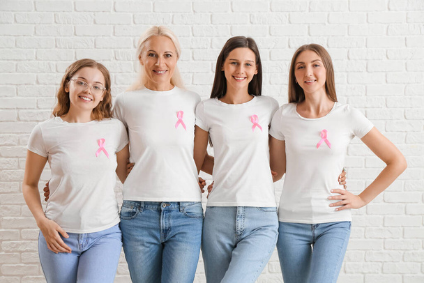 Красивые женщины с розовыми лентами осознания обнимаются на белом кирпичном фоне. Концепция рака молочной железы - Фото, изображение