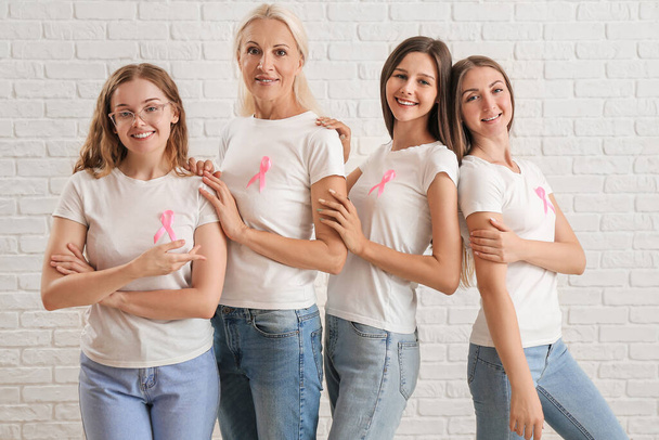 Belle donne con nastri di consapevolezza rosa su sfondo di mattoni bianchi. Concetto di cancro al seno - Foto, immagini