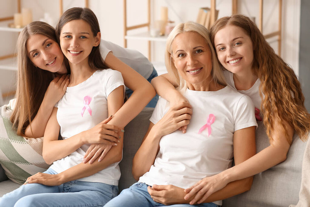 Beautiful women with pink awareness ribbons hugging on sofa at home. Breast cancer concept - Photo, Image