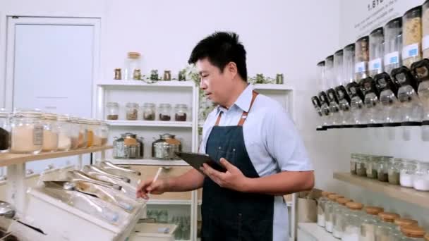 Asiatische männliche Ladenbesitzer überprüft Lager von Bioprodukten in den Regalen der Nachfüllläden, Null-Abfall-und nachhaltige Shop, thailändische Schriftzüge an der Wand bedeuten "füllen Sie einen Behälter mit allen Massengütern" - Filmmaterial, Video