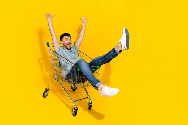 Full length portrait of overjoyed surprised man sit market trolley look empty space isolated on yellow color background. - Фото, зображення