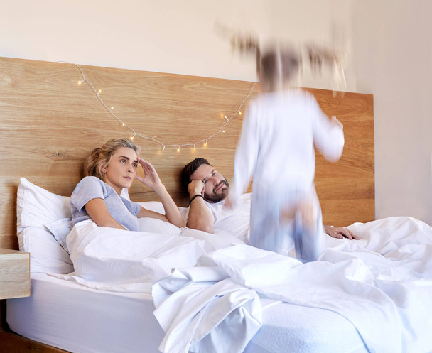 Exhausted parents struggling to put hyperactive toddler child to bed. Tired mom and dad annoyed about noisy active daughter jumping on their bed. - Fotoğraf, Görsel