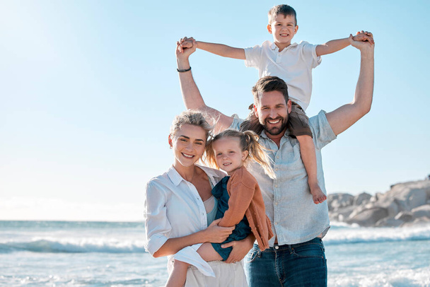 Portrait of happy caucasian parents and kids sharing quality time while enjoying a fun family summer vacation at the beach. Loving mom and dad holding and bonding with their little son and daughter. - 写真・画像