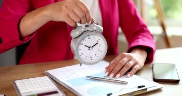 Hand der Geschäftsfrau hält Wecker für zehn Uhr, während sie am Schreibtisch sitzt. Arbeitszeitmanagement-Konzept - Filmmaterial, Video