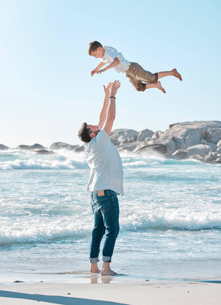 Single dad playing with son on the beach during the day. Caucasian single father bonding his son and throwing him in the air before catching him. Cute little boy enjoying free time with his parent. - Photo, Image