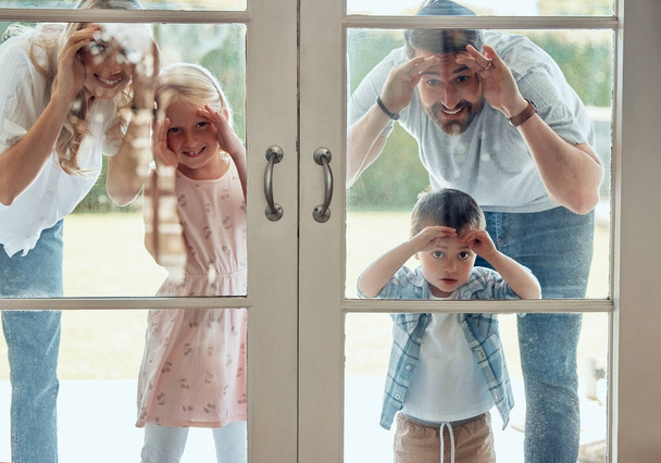 Любопытная пара с маленькими детьми, стоящими и заглядывающими в их новый дом. Возбужденная улыбающаяся кавказская семья смотрит и проверяет свой дом от двери. Очаровательный мальчик и девочка со своими родителями. - Фото, изображение