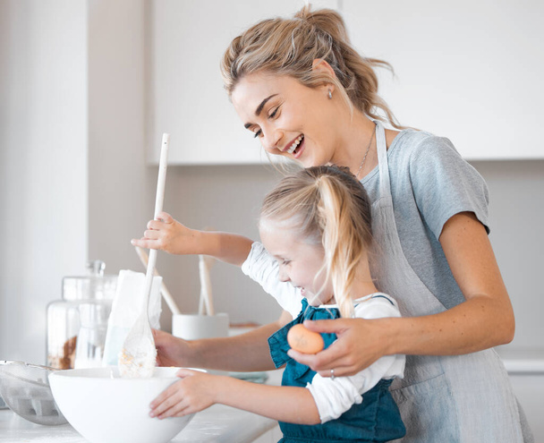 Mother helping her daughter bake. Happy woman holding an egg helping her child bake. Little girl mixing a bowl of batter. Small child bonding with her mother and cooking together.Happy family baking. - Zdjęcie, obraz