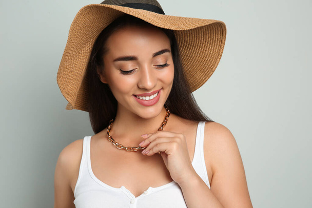 Όμορφη νεαρή γυναίκα που φοράει ψάθινο καπέλο σε ανοιχτό γκρι φόντο. Κομψό φόρεμα κεφαλής - Φωτογραφία, εικόνα