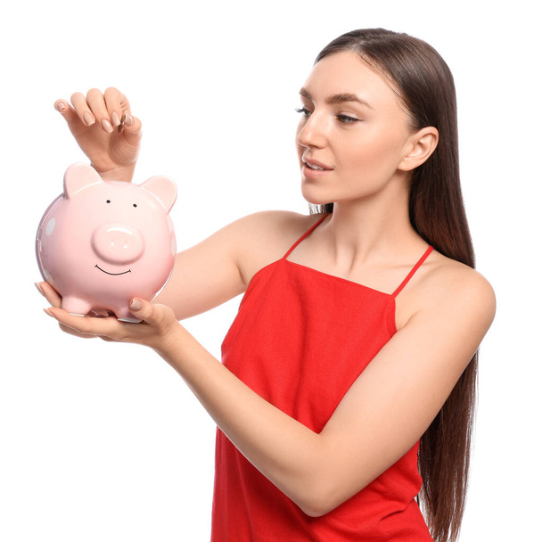 Young woman putting coin into piggy bank on white background - Foto, Imagem