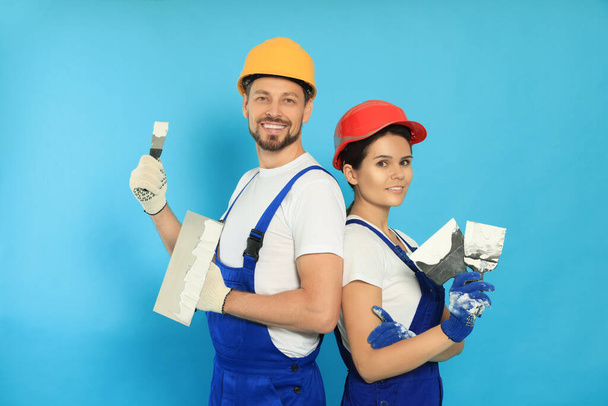 Professional workers with putty knives in hard hats on light blue background - Valokuva, kuva