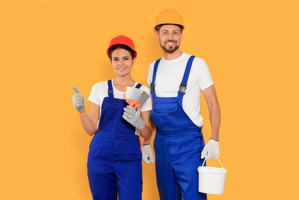 Professional workers with putty knives and plaster in hard hats on orange background - Foto, immagini