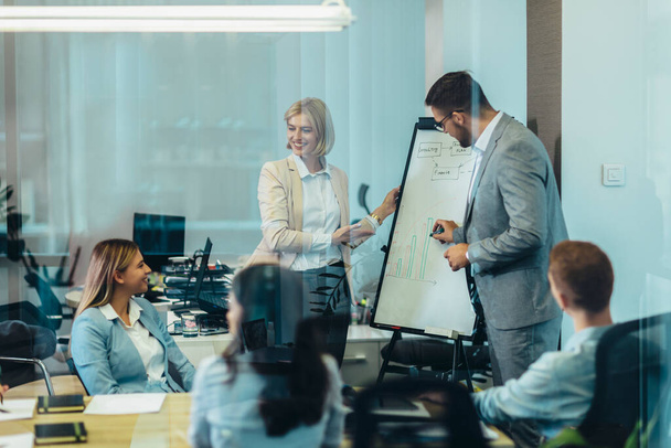 Επιχειρηματίες δίνουν μια παρουσίαση στους συναδέλφους της σε ένα λευκό πίνακα σε μια αίθουσα συνεδριάσεων - Φωτογραφία, εικόνα