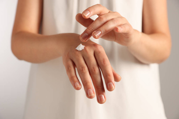 Woman applying cosmetic cream onto hand against light grey background, closeup - Фото, изображение