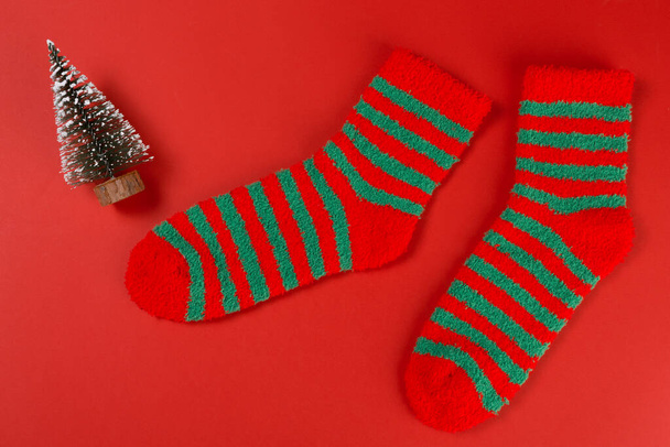 Two green striped Christmas socks, as if walking, next to the Christmas tree, concept, on a red background, flat lay - Photo, Image