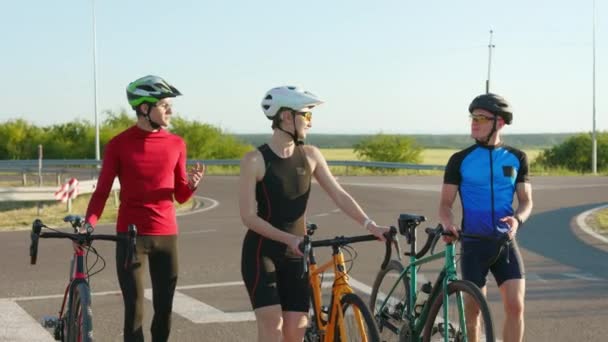 Gelukkig blanke vrouw en twee mannen lopen op asfaltweg met gekleurde fietsen. Professionele fietsers met sportkleding, veiligheidshelmen en bril. - Video
