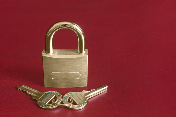 A closed gold padlock on a red studio background along with a pair of keys decorated with turquoise blue shapes and copy space. Security and trust concept. - Photo, Image