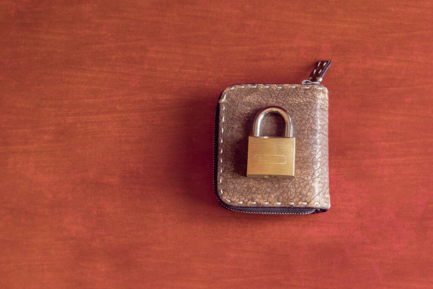 Un cadenas fermé sur un portefeuille en cuir zippé sur un fond studio coloré avec texture et espace de copie. Concept de sécurité et de finance. - Photo, image